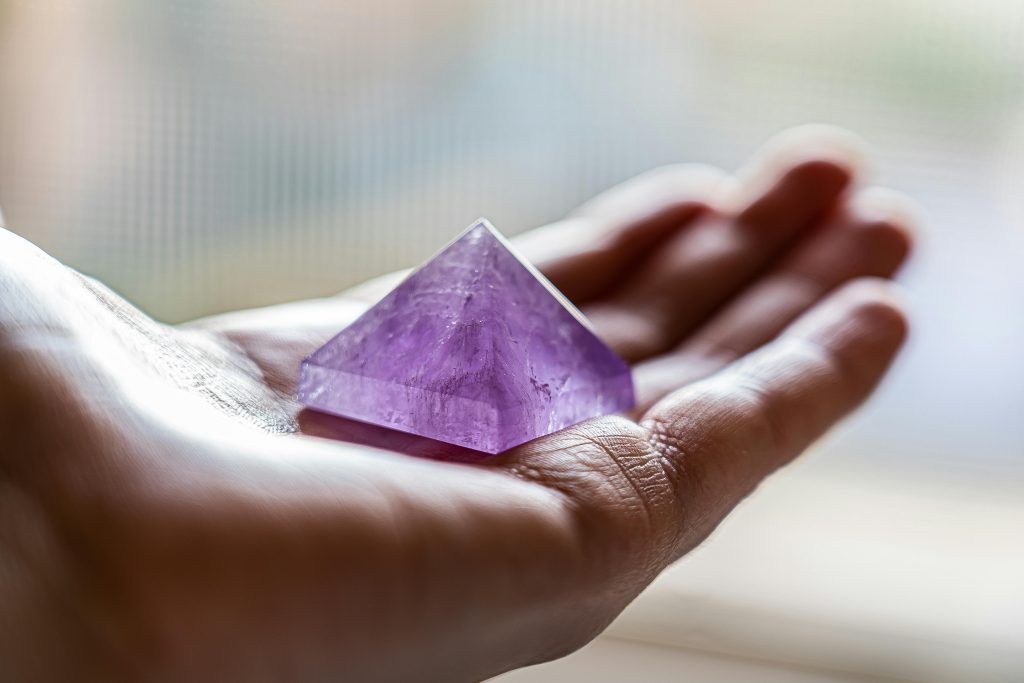 Close-up of an amethyst pyramid crystal resting in an open hand, captured in soft lighting.